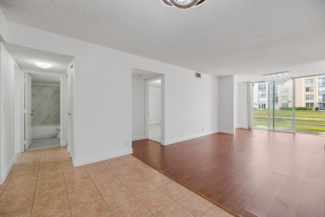 spare room with light tile patterned flooring, a wall of windows, a textured ceiling, and a chandelier