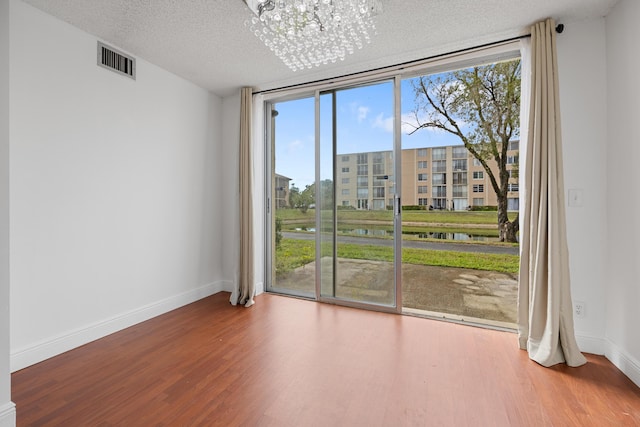 empty room with a chandelier, wood-type flooring, a textured ceiling, and floor to ceiling windows