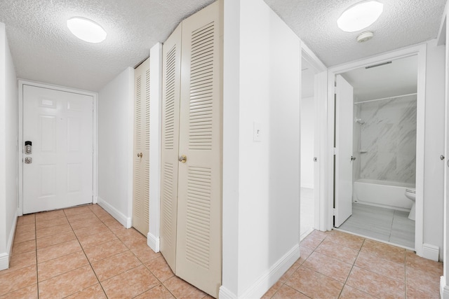 hallway with a textured ceiling and light tile patterned flooring