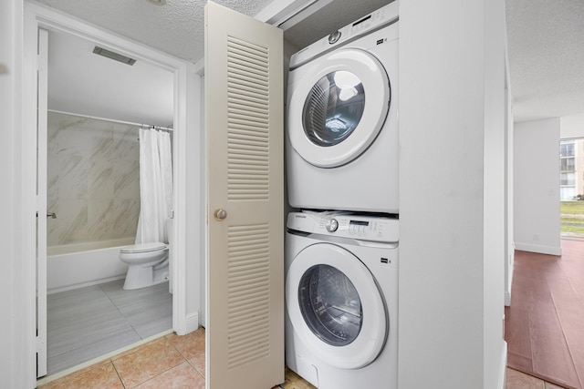 washroom featuring light tile patterned floors, a textured ceiling, and stacked washing maching and dryer