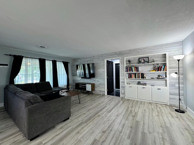 living room featuring built in shelves, wood walls, a textured ceiling, and light wood-type flooring