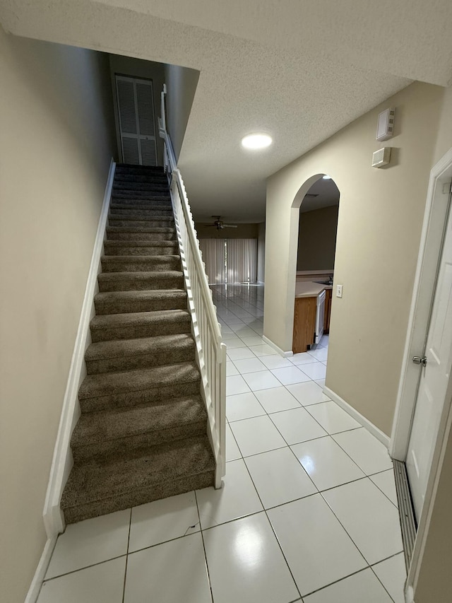 stairs featuring ceiling fan, tile patterned flooring, and a textured ceiling