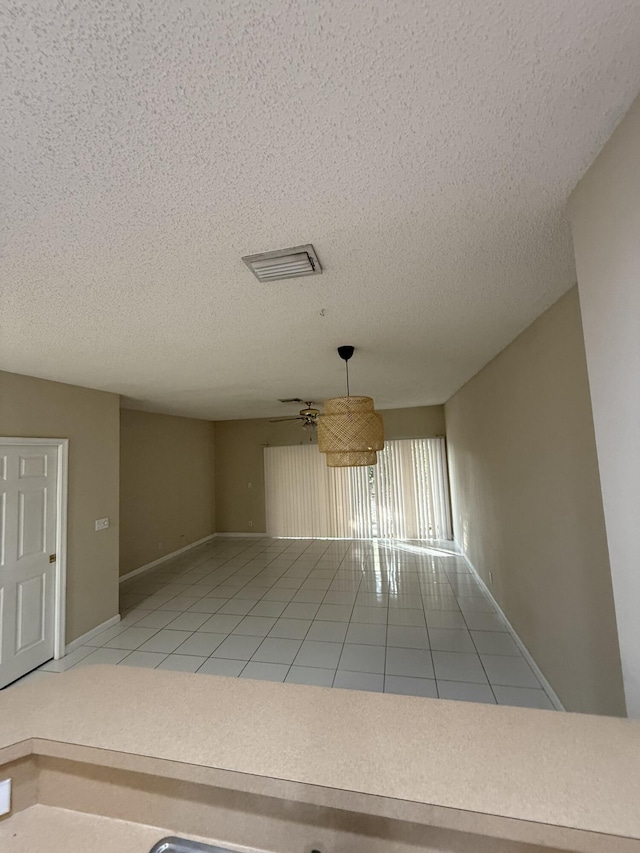 spare room featuring ceiling fan, light tile patterned flooring, and a textured ceiling