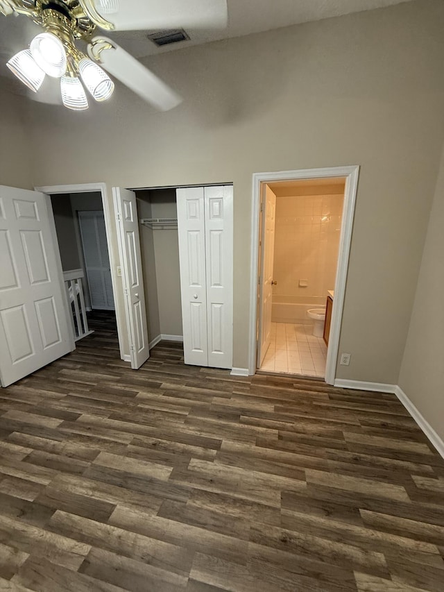 unfurnished bedroom with ensuite bathroom, ceiling fan, dark wood-type flooring, and a high ceiling