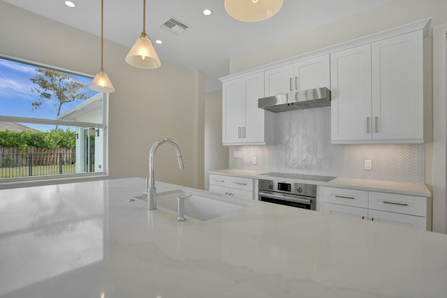 kitchen featuring white cabinets, sink, hanging light fixtures, stainless steel oven, and light stone counters