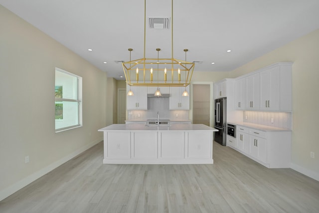 kitchen featuring sink, an island with sink, high quality fridge, and white cabinetry