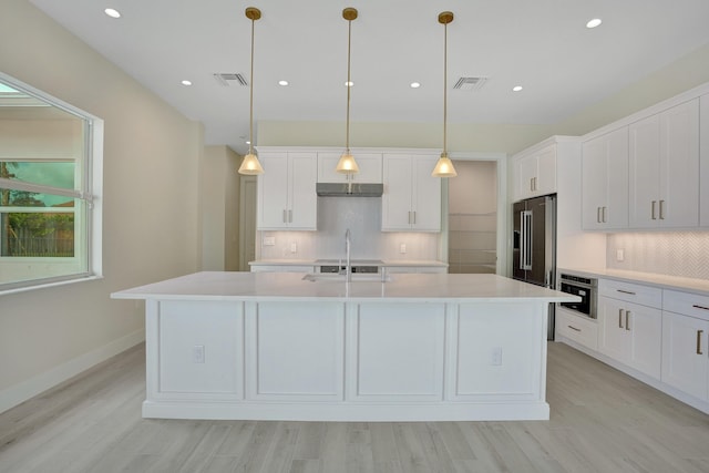 kitchen featuring white cabinetry, appliances with stainless steel finishes, a kitchen island with sink, light wood-type flooring, and decorative light fixtures