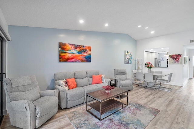 living room featuring light wood-type flooring, a textured ceiling, and vaulted ceiling