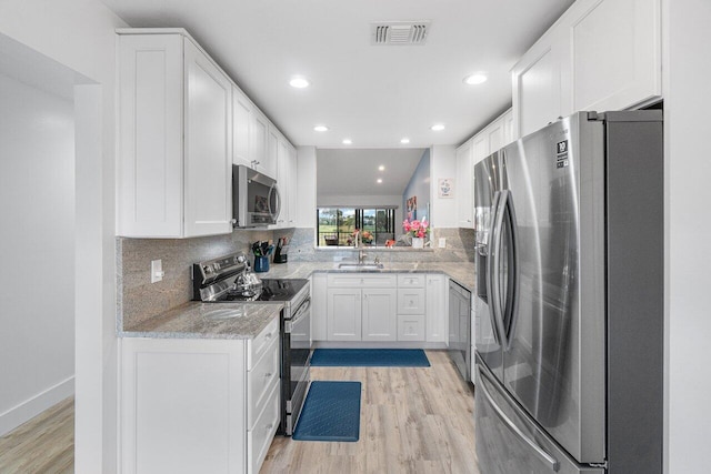 kitchen featuring tasteful backsplash, vaulted ceiling, light wood-type flooring, appliances with stainless steel finishes, and white cabinets