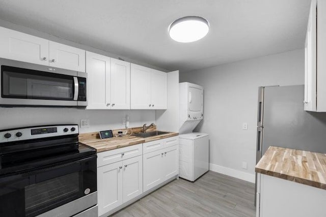 kitchen featuring sink, stacked washer and dryer, appliances with stainless steel finishes, butcher block countertops, and white cabinetry