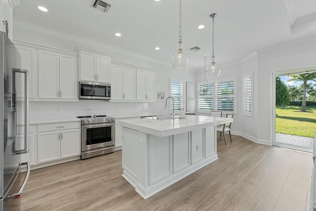 kitchen with a wealth of natural light, hanging light fixtures, an island with sink, white cabinets, and appliances with stainless steel finishes