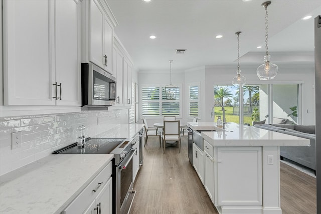 kitchen with stainless steel appliances, an island with sink, pendant lighting, white cabinetry, and backsplash