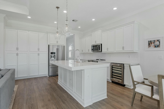 kitchen featuring decorative light fixtures, beverage cooler, a kitchen island with sink, white cabinetry, and appliances with stainless steel finishes