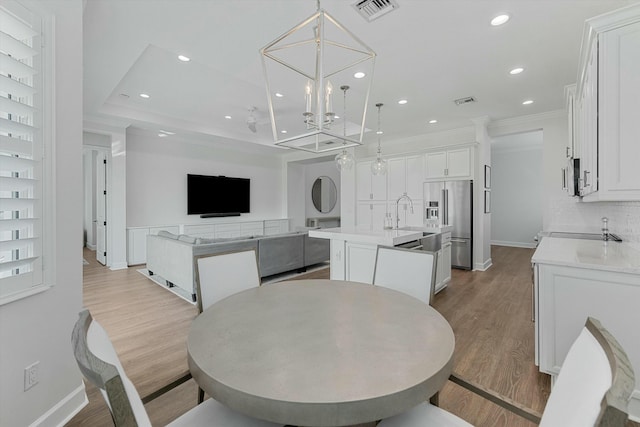 dining area with a notable chandelier, light hardwood / wood-style flooring, ornamental molding, and a raised ceiling