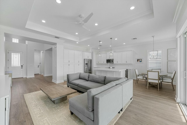 living room featuring a raised ceiling, light wood-type flooring, and ceiling fan