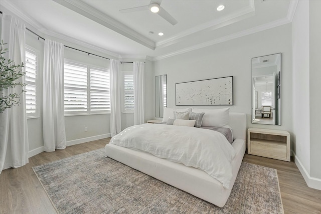 bedroom with ceiling fan, light wood-type flooring, crown molding, and a tray ceiling