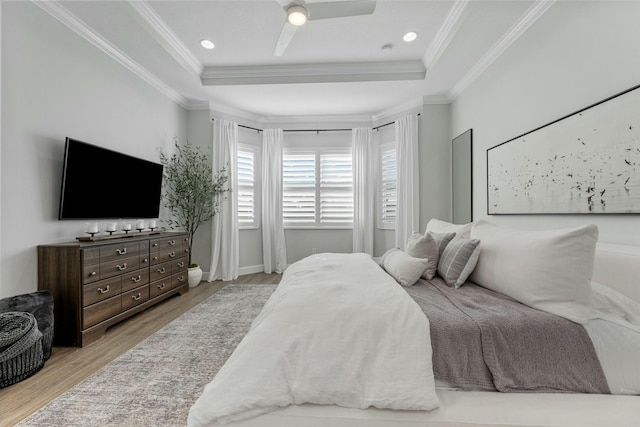 bedroom with ornamental molding, light wood-type flooring, ceiling fan, and a tray ceiling