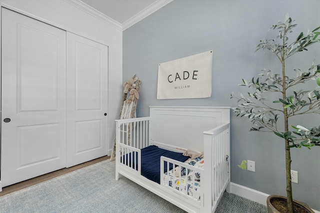 bedroom featuring a crib, a closet, crown molding, and wood-type flooring