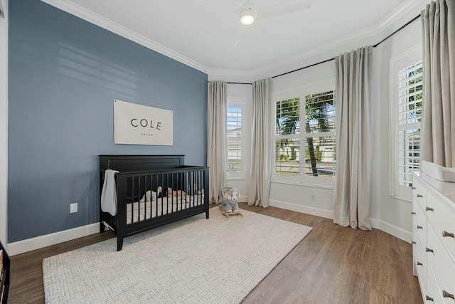 bedroom featuring a nursery area, ceiling fan, light hardwood / wood-style floors, and crown molding