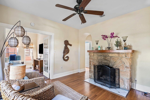 living room featuring dark hardwood / wood-style floors, a stone fireplace, and ceiling fan