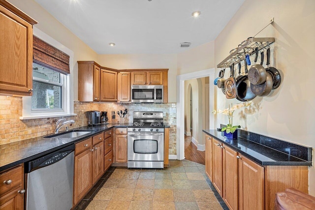 kitchen featuring backsplash, sink, dark stone counters, and appliances with stainless steel finishes