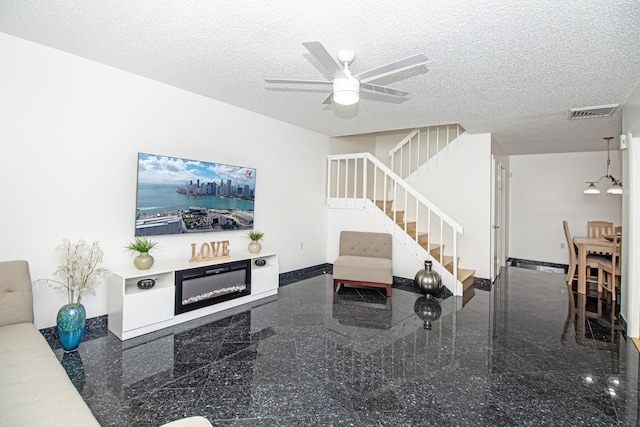 living room featuring ceiling fan with notable chandelier and a textured ceiling