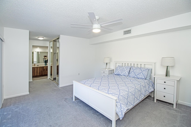 bedroom with ceiling fan, light colored carpet, ensuite bathroom, and a textured ceiling