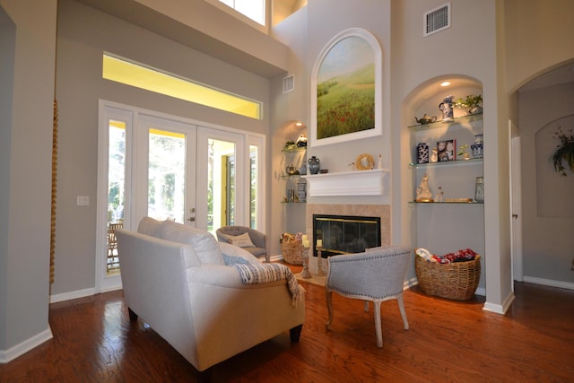 living room featuring a tile fireplace, french doors, a high ceiling, dark hardwood / wood-style flooring, and built in features