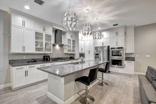 kitchen featuring sink, dark stone countertops, a kitchen island with sink, stainless steel appliances, and wall chimney exhaust hood