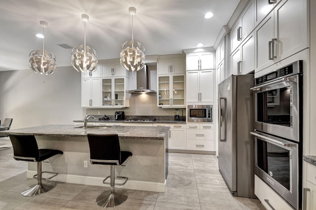 kitchen with wall chimney exhaust hood, a breakfast bar, light stone counters, an island with sink, and stainless steel appliances