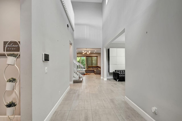 corridor featuring light tile patterned floors, a towering ceiling, and a chandelier