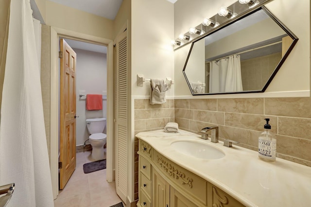 bathroom with toilet, vanity, tile patterned floors, and tile walls