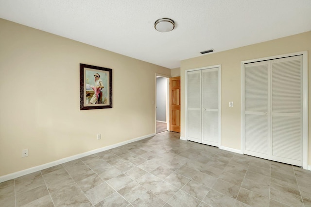 unfurnished bedroom featuring a textured ceiling and two closets