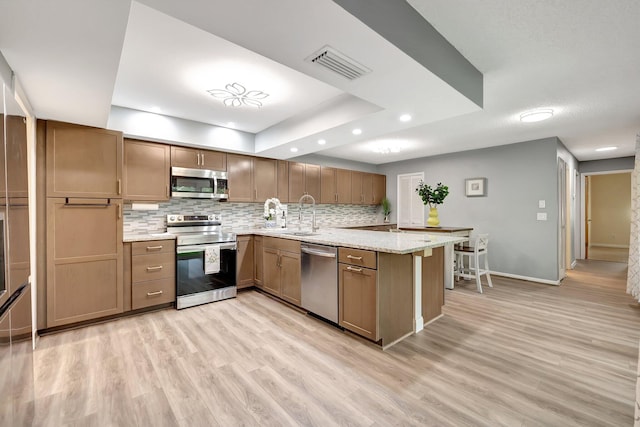 kitchen with sink, light stone counters, kitchen peninsula, appliances with stainless steel finishes, and light wood-type flooring