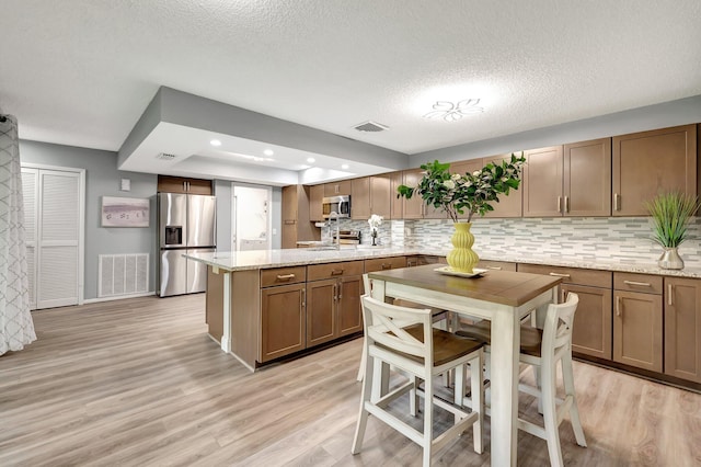 kitchen featuring appliances with stainless steel finishes, light stone counters, a textured ceiling, a raised ceiling, and light hardwood / wood-style flooring