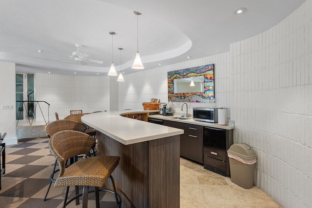 kitchen featuring ceiling fan, sink, a raised ceiling, pendant lighting, and a kitchen bar