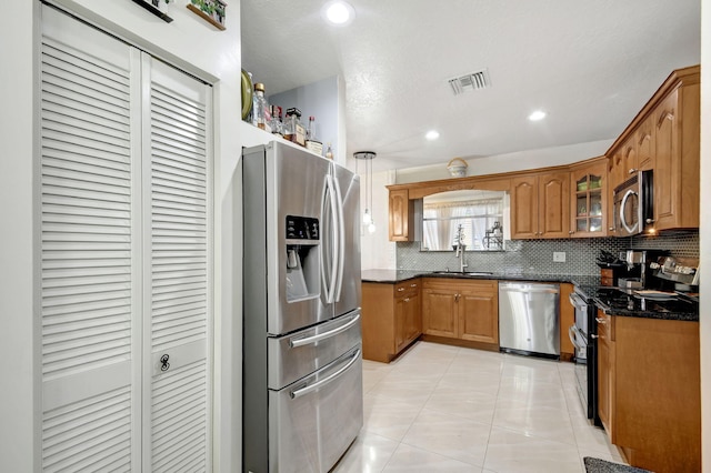 kitchen featuring light tile patterned floors, appliances with stainless steel finishes, tasteful backsplash, dark stone counters, and sink