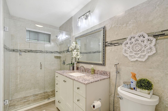 bathroom with a shower with shower door, vanity, tile walls, and toilet