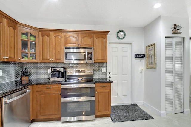 kitchen featuring light tile patterned floors, decorative backsplash, dark stone counters, and stainless steel appliances