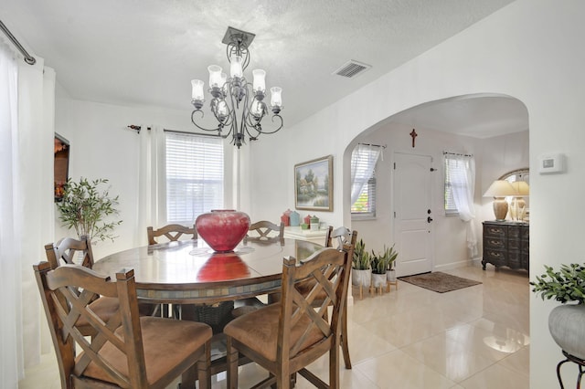 dining area with a textured ceiling, an inviting chandelier, a wealth of natural light, and light tile patterned flooring