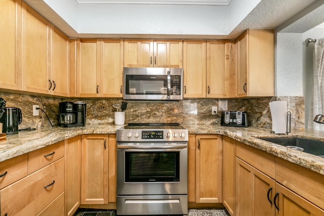 kitchen with backsplash, light stone countertops, sink, and appliances with stainless steel finishes