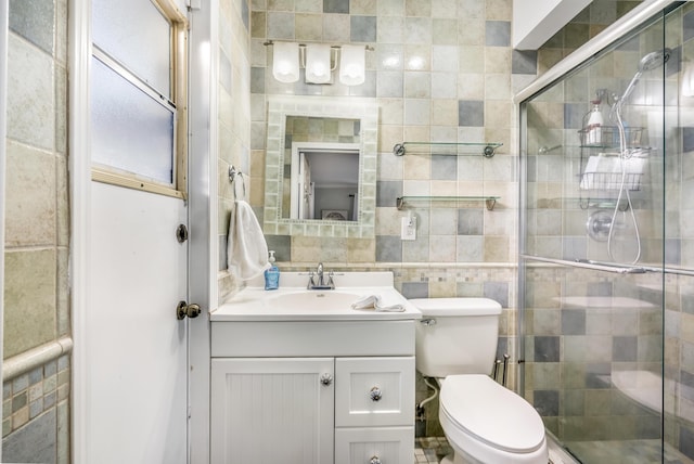 bathroom with vanity, toilet, a shower with door, and tile walls