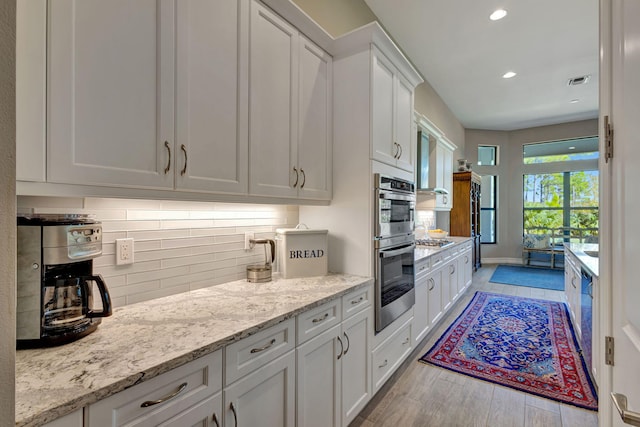 kitchen featuring backsplash, light stone countertops, white cabinets, and stainless steel appliances