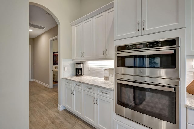 kitchen with white cabinetry, tasteful backsplash, light wood-type flooring, double oven, and light stone countertops