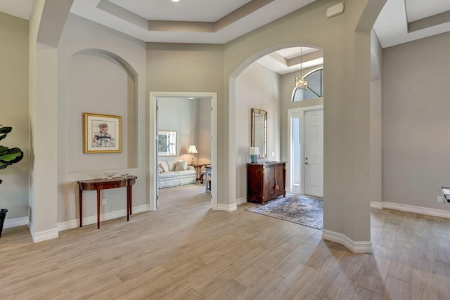 entryway with an inviting chandelier, a tray ceiling, light hardwood / wood-style flooring, and a high ceiling