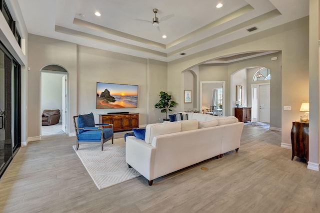 living room with ceiling fan, a towering ceiling, a tray ceiling, and light hardwood / wood-style flooring