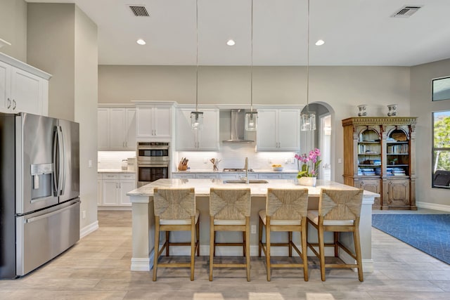 kitchen featuring white cabinetry, stainless steel appliances, an island with sink, and hanging light fixtures