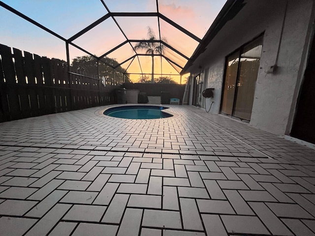 pool at dusk featuring a lanai and a patio