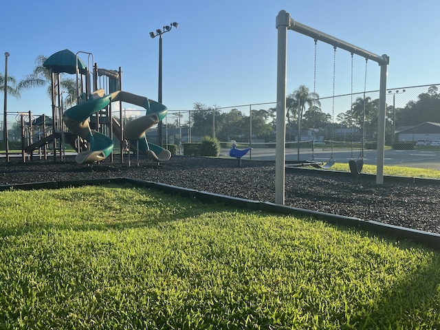 view of jungle gym with tennis court and a lawn