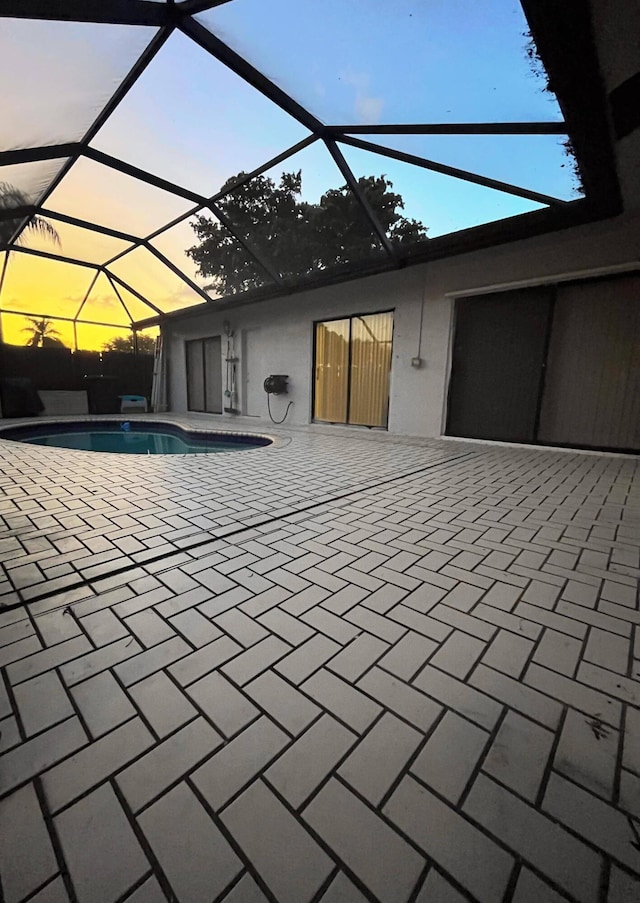 pool at dusk with a lanai and a patio